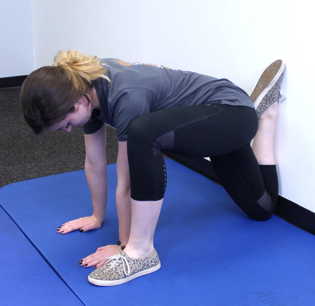 Woman performing wall knee stretch with foot balanced