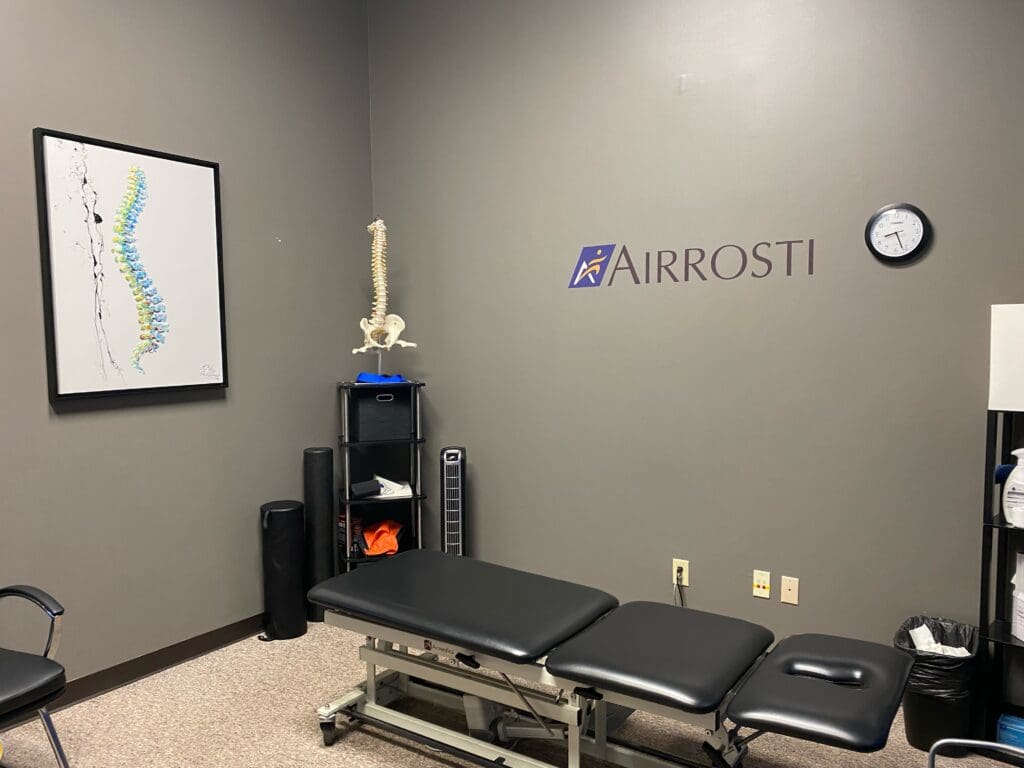 Photo of the treatment room at Airrosti Far Hills. Photo included the Airrosti Logo and the treatment table.
