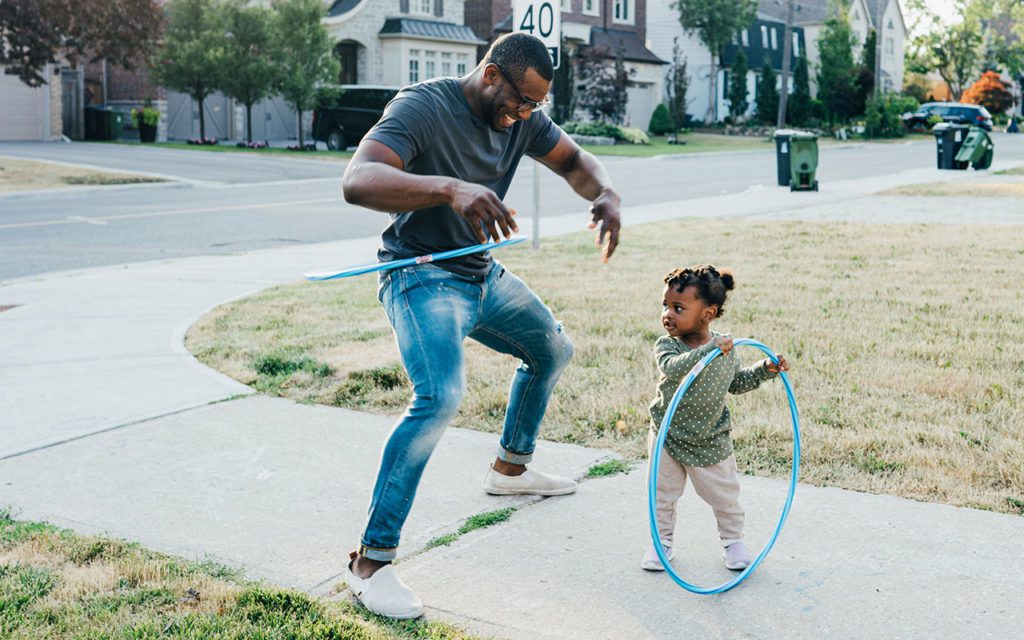 Parent smiling and using hula hoop outdoors with child