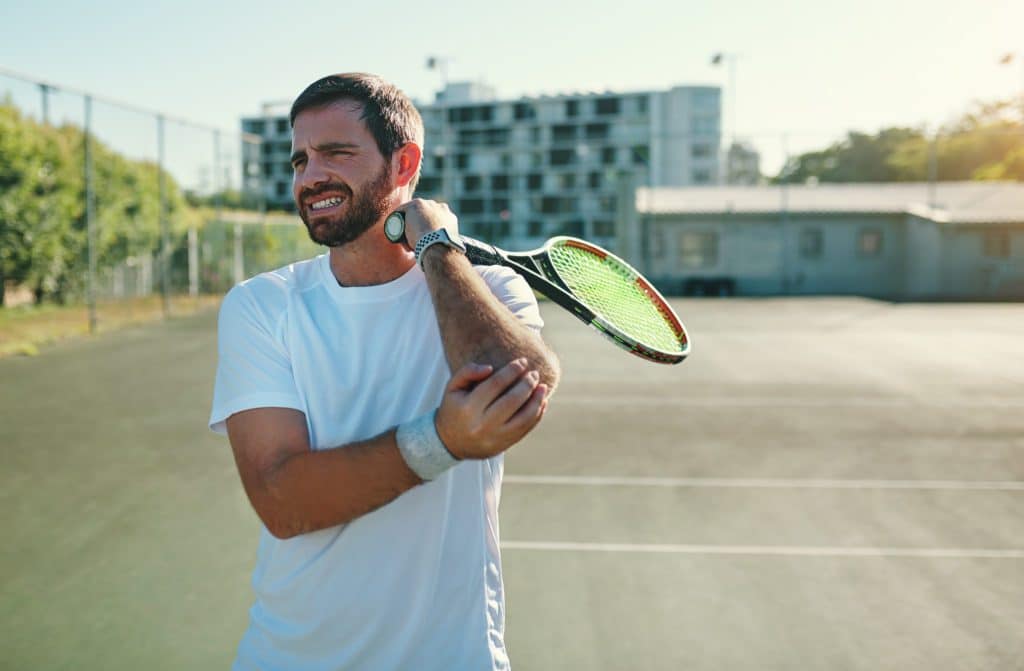 guy holding a tennis racket rubbing his elbow