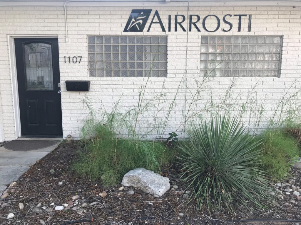 A closer look at the front entrance leading to Airrosti Bastrop, showing the number 1107 and the Airrosti logo near the door.