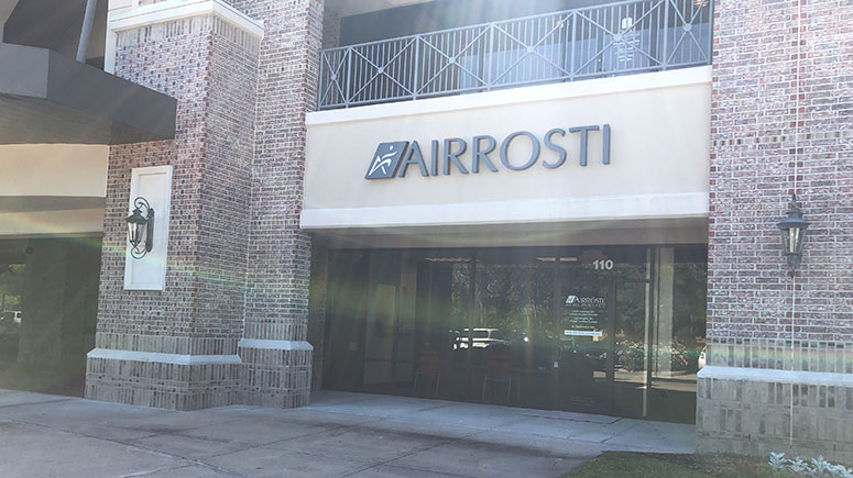 Photo of the exterior front entrance of Airrosti Cinco Ranch. The Airrosti logo is visible above the glass doors that lead into the practice