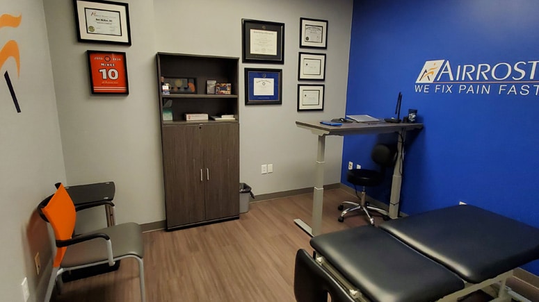 a photo of the treatment room at Airrosti West Plano. The Airrosti Provider's accolades decorate the wall