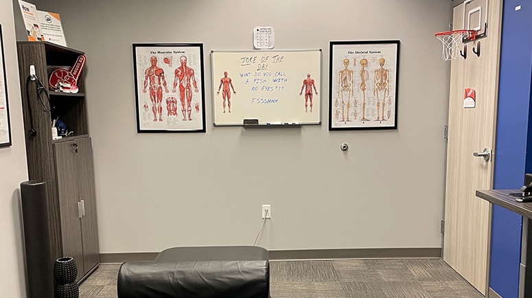 Photo of the inside of the treatment room at Airrosti Downtown Tunnels. Photo includes the treatment table and MSK diagrams decorate the wall