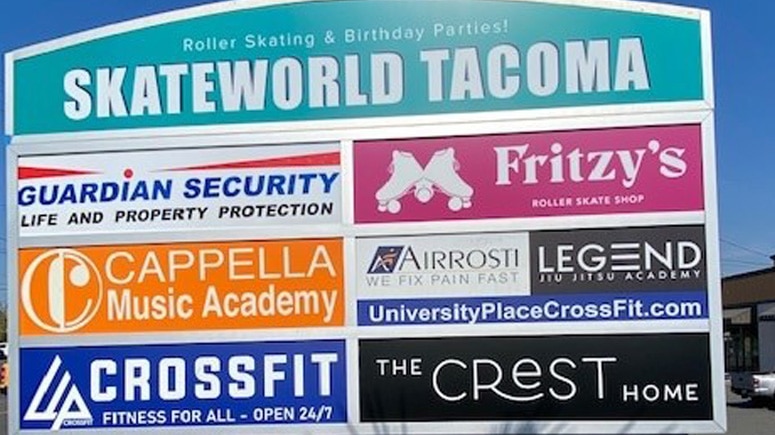A view of the outdoor shopping center signage, showing Airrosti Tacoma alongside its business neighbors, Skateworld Tacoma, Fritz Skate Shop, etc.