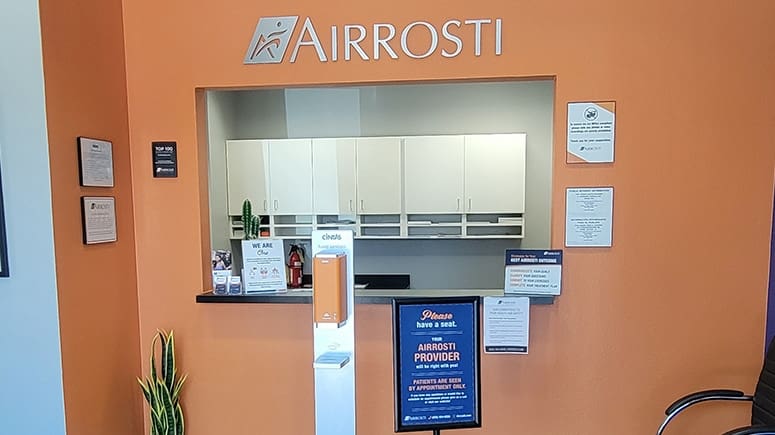 a photo of the check in window inside the lobby at Airrosti McKinney. Airrosti logo is visible above the wall opening. There is a small office behind the window.