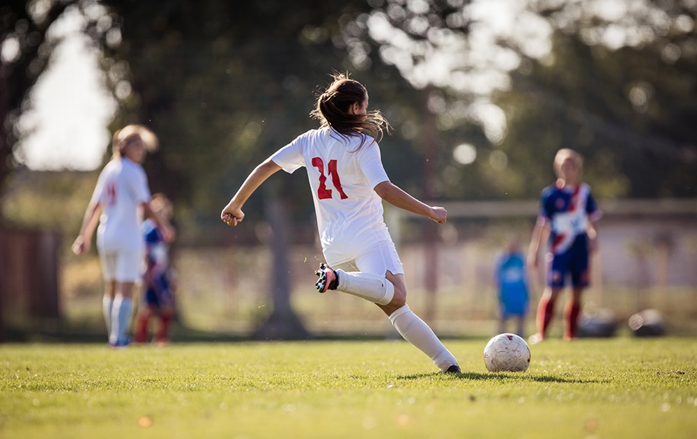 Rear view of determined female soccer player kicking the ball on a match.