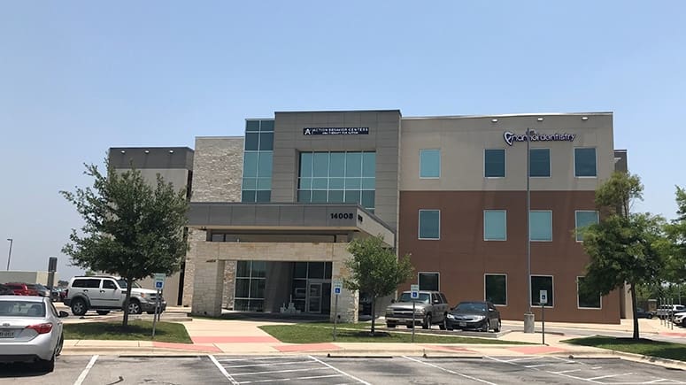 A wide view of the building exterior where Airrosti Manor is located. A large medical office building with the Medical Towers at Shadowglen sign visible from a distance on the upper side of the building.