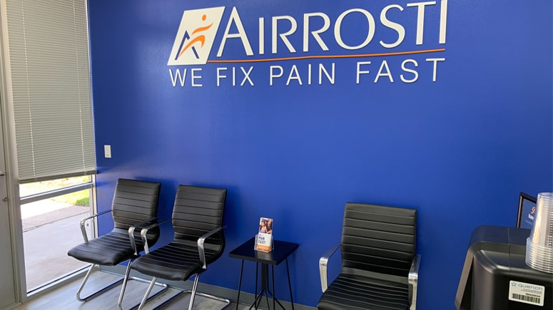 A view of the lobby inside Airrosti Space Center, showing chairs for patron use and the Airrosti logo painted on the wall