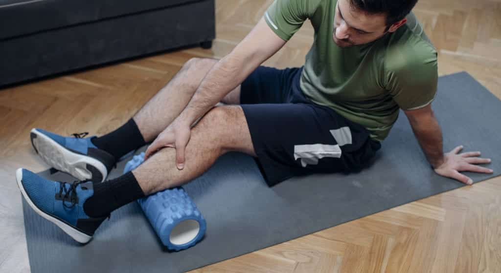 Foam Roller Massage after a Home Workout: a Man in Sportswear Relaxing his Muscles after Exercising in the Living Room