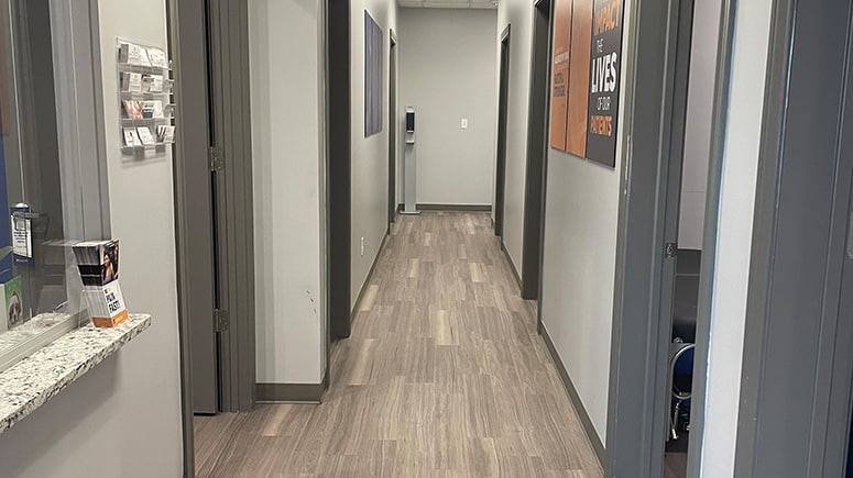 a photo of the hallway inside Airrosti Carrollton. Airrosti posters decorate the walls. Treatment and recovery room doors are visible