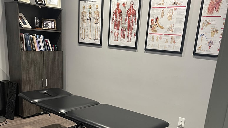 a photo showing the treatment room at Airrosti Carrollton. Musculoskeletal diagrams decorate the wall