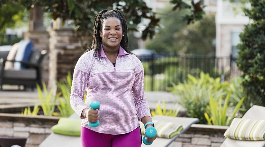 Pregnant woman exercising outside while smiling.