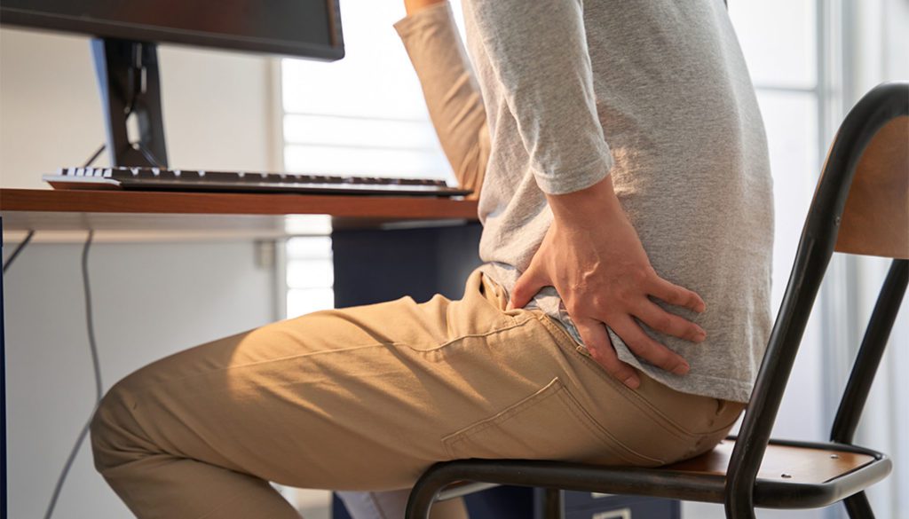 man holding his hip sitting at a desk