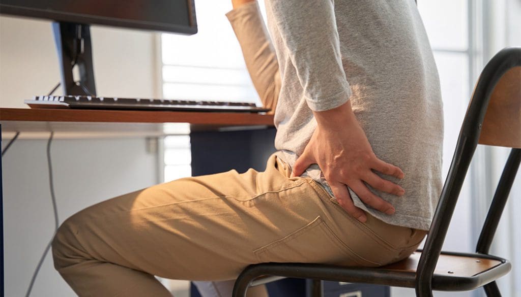 man holding his hip sitting at a desk