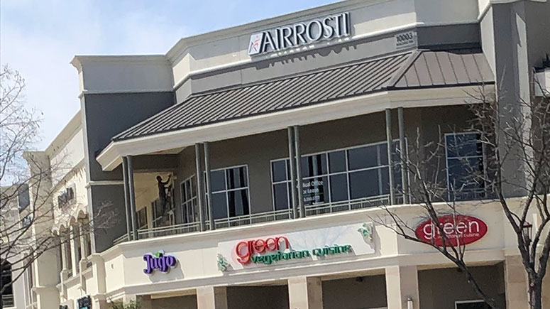An exterior view of the building at Airrosti Alon Market, showing the Airrosti sign on the second floor above two other businesses