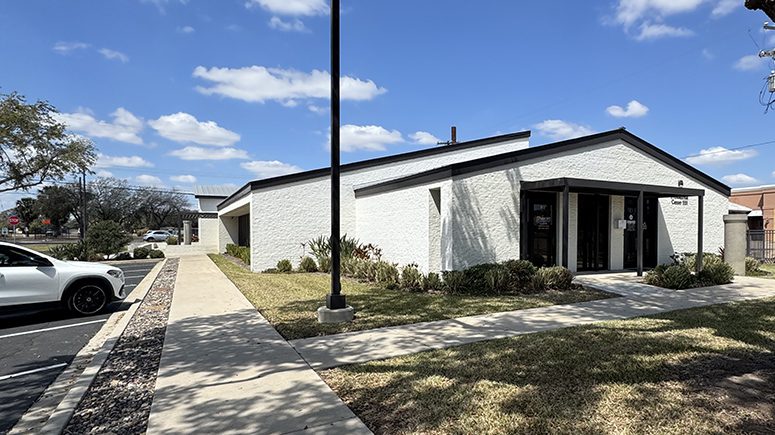 A wide shot of the building exterior of Airrosti Weslaco, showing a white, single story building with a black roof.