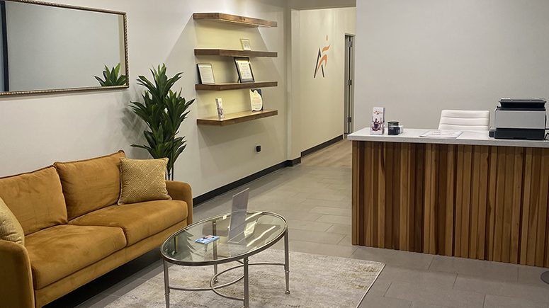 A view of the interior of the lobby at Airrosti Weslaco. A sofa and coffee table can been seen next to the check in counter.