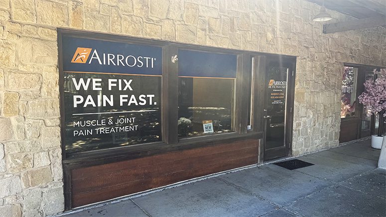 A view of the building exterior where Airrosti Cedar Hill is located. Large glass windows and a front door can be seen in a light colored stone facade.